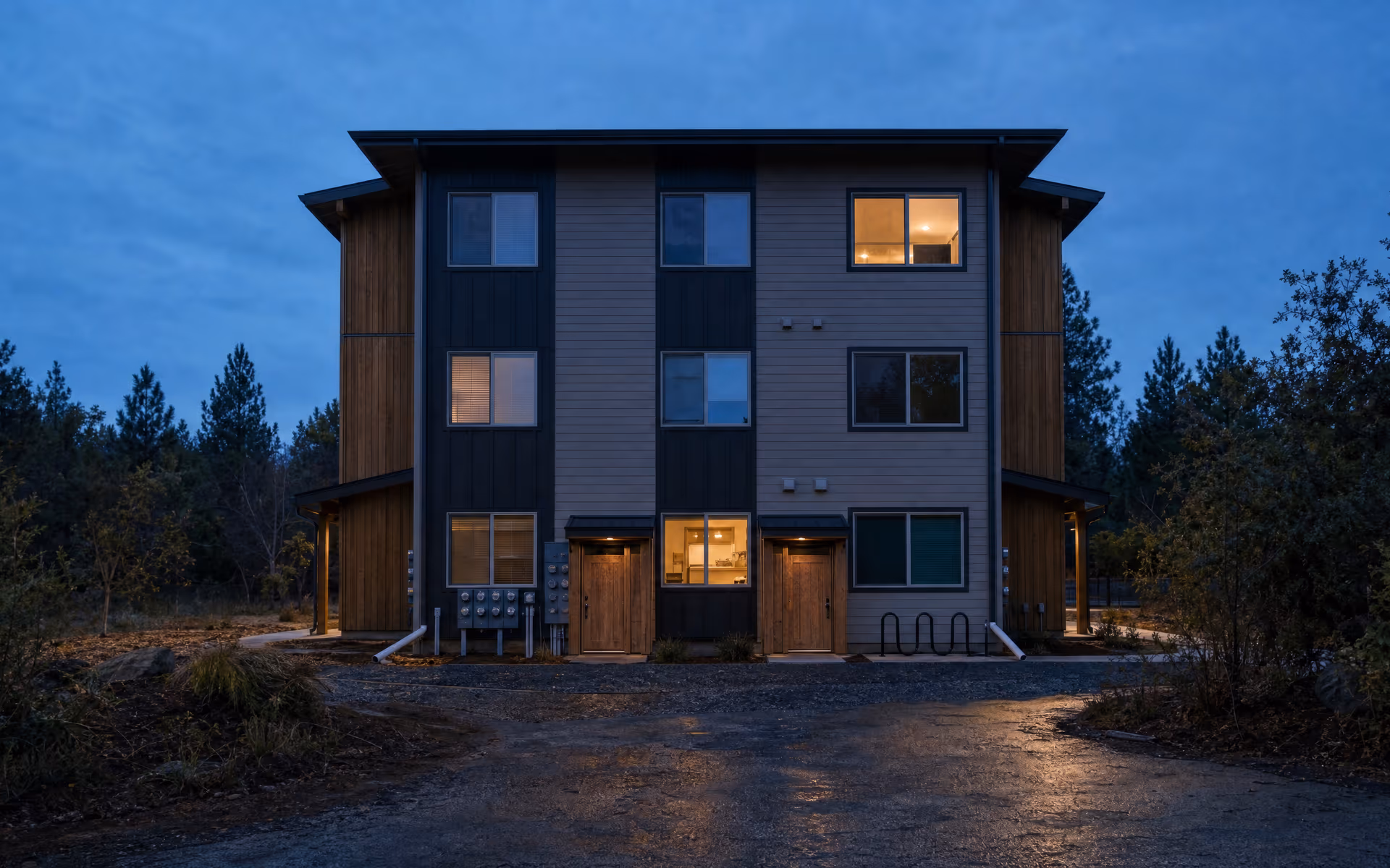 Conceptual rendering of a three-story Southern Oregon multifamily building at blue hour, seen head on. Not a real customer property.