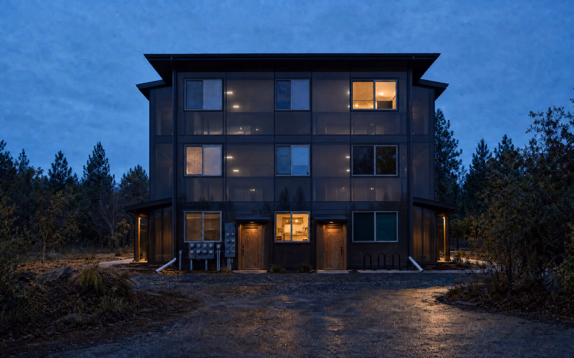 Conceptual rendering of the same three-story multifamily building with its envelope rendered as smoked glass, floor plates faintly visible, a warm glow at the ground-floor service room.