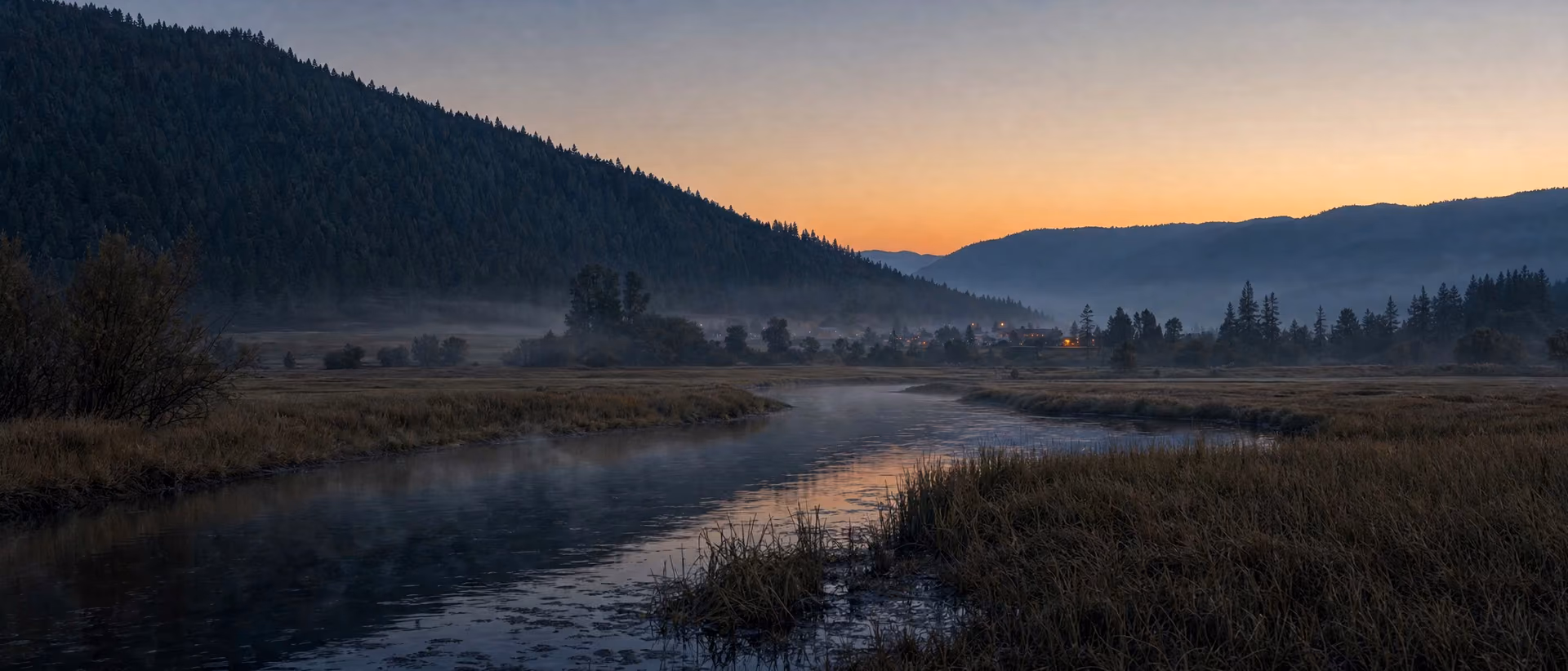 Conceptual rendering: dawn on the river flats of a Southern Oregon valley, fog over the water, a small town's lights at the far end below the ridge.